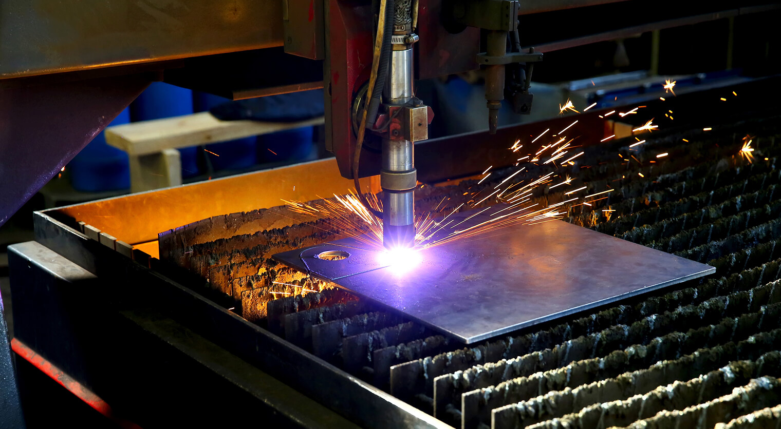 Automated plasma cutting torch creating bright sparks while cutting metal sheet on CNC table in industrial workshop.