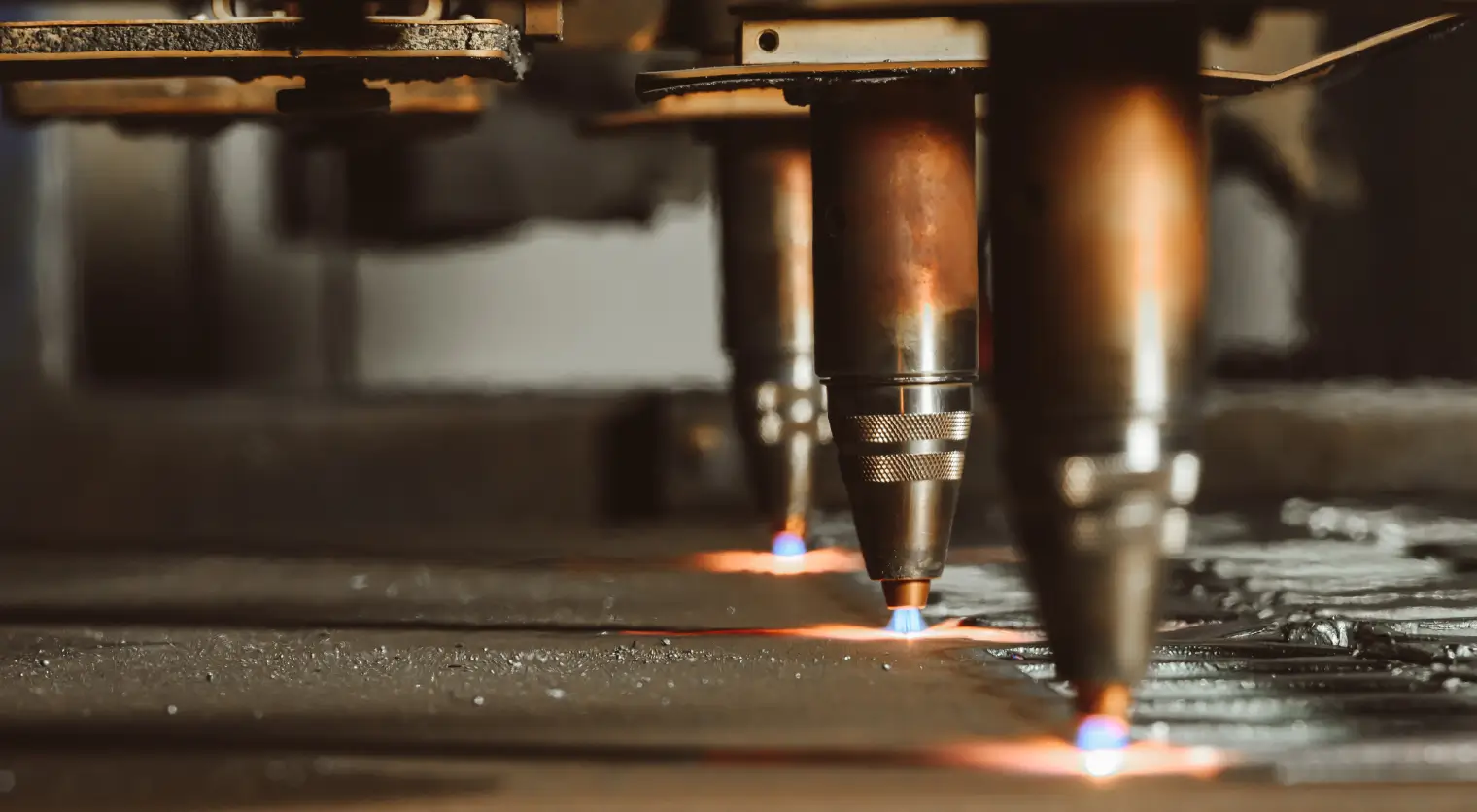 Multiple copper-colored CNC plasma cutting torches with blue flames cutting metal sheet in industrial manufacturing environment.