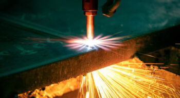CNC plasma cutter cutting through metal sheet with bright orange sparks flying during industrial fabrication process.