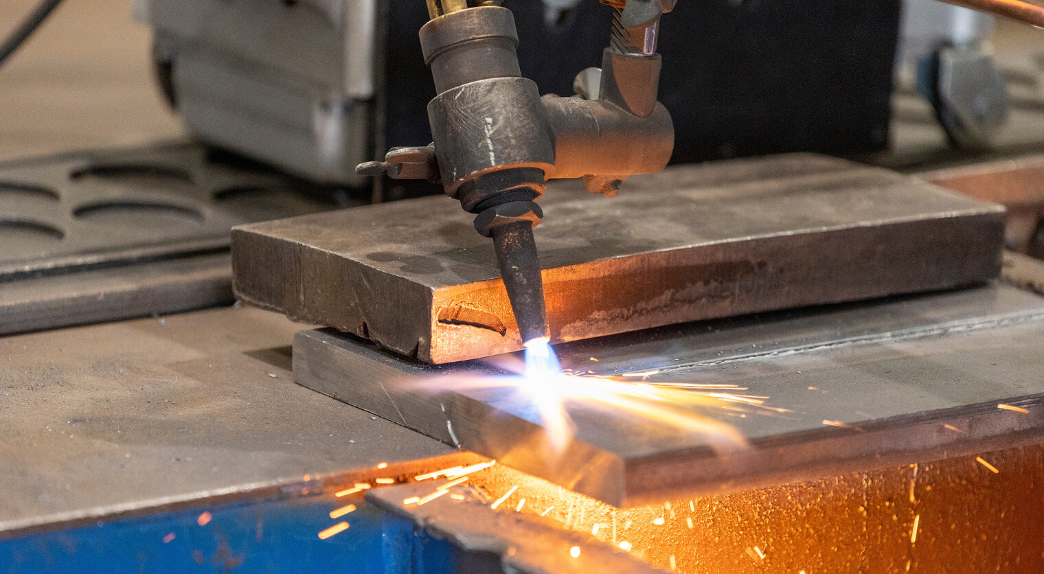 Oxyfuel cutting torch cutting thick carbon steel plate on a CNC table with sparks below the cut