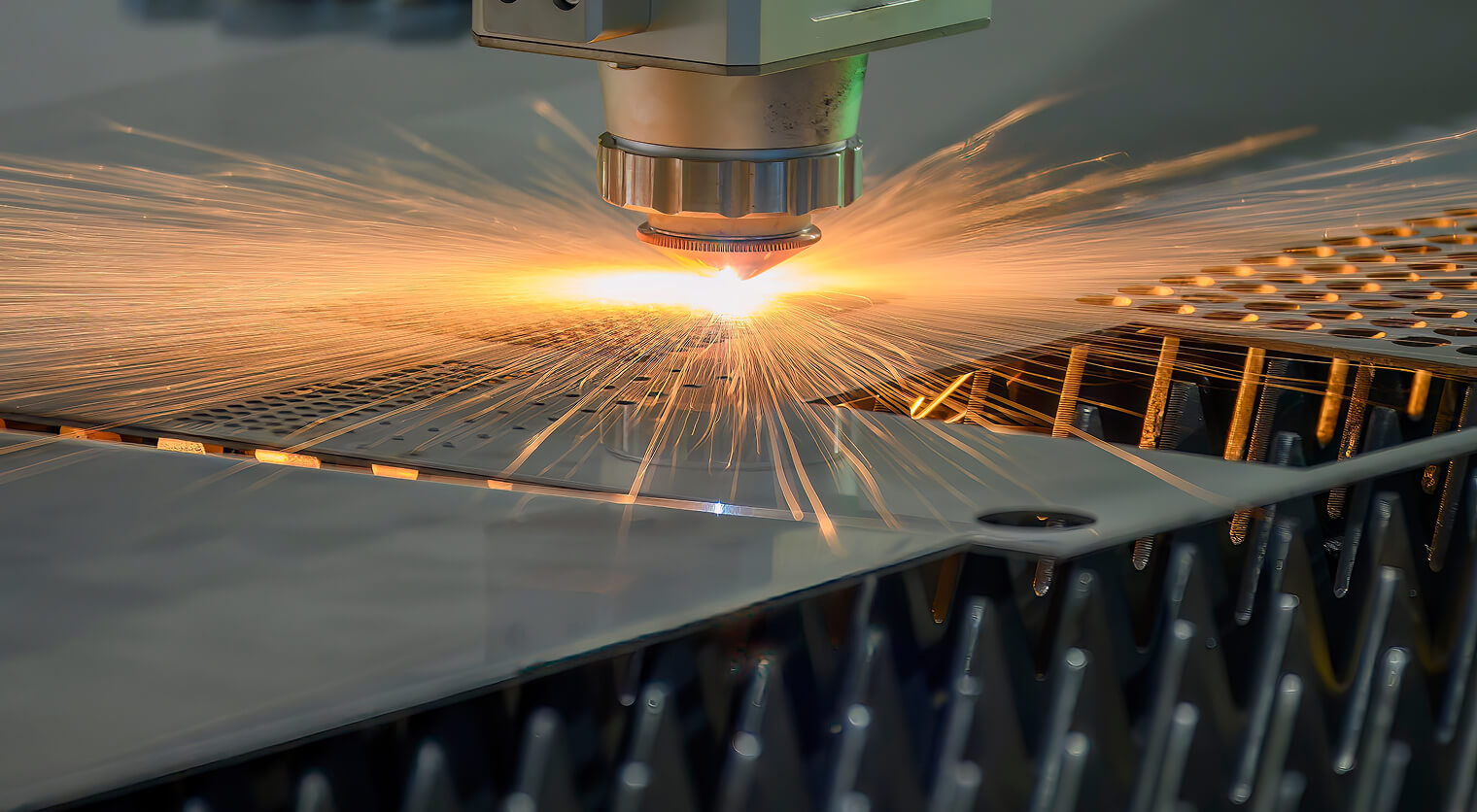 Fiber laser cutting head cutting thin sheet metal with sparks spraying across a slatted cutting bed